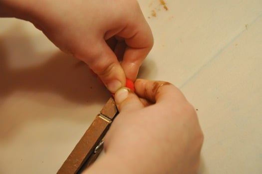 child gluing red ball on clothespin