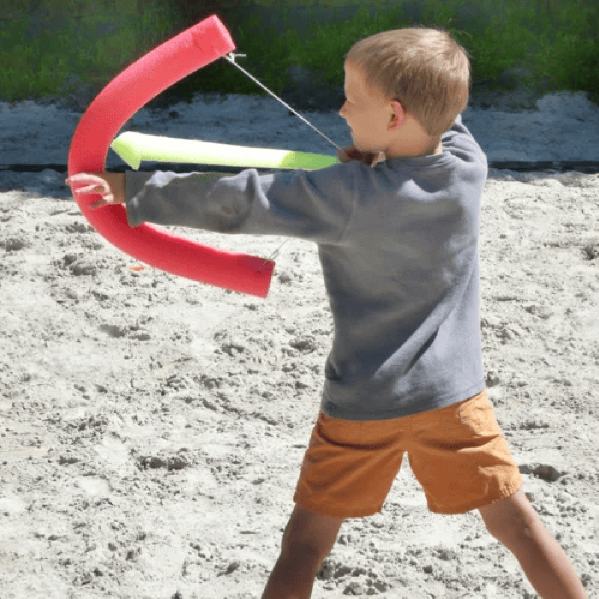 Pool Noodle Activities- boy holding faux bow and arrow in sand- Kids Activities Blog