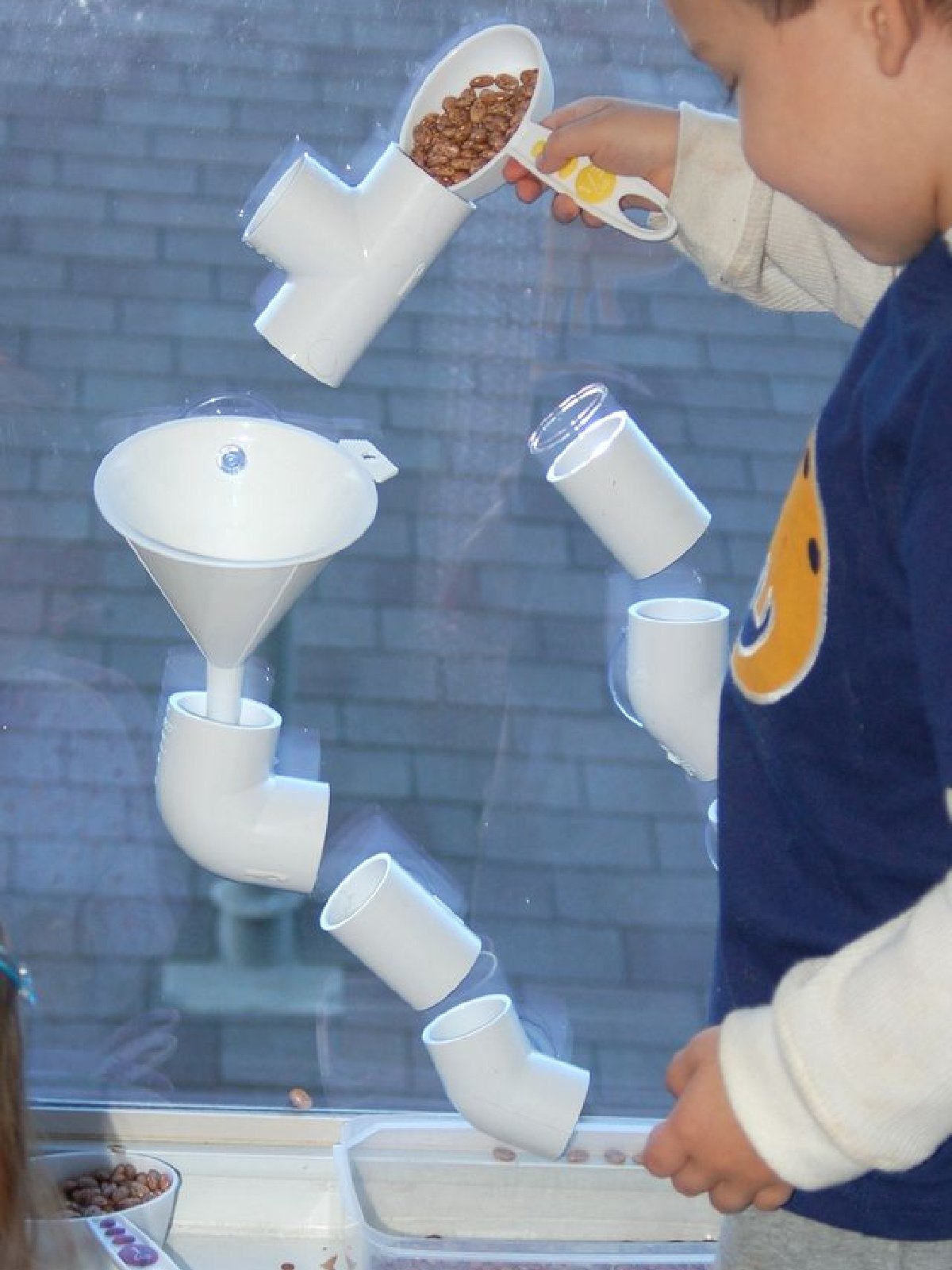 Tube Play- Boy pouring beans in pvc tubes stuck on window- kids activities blog