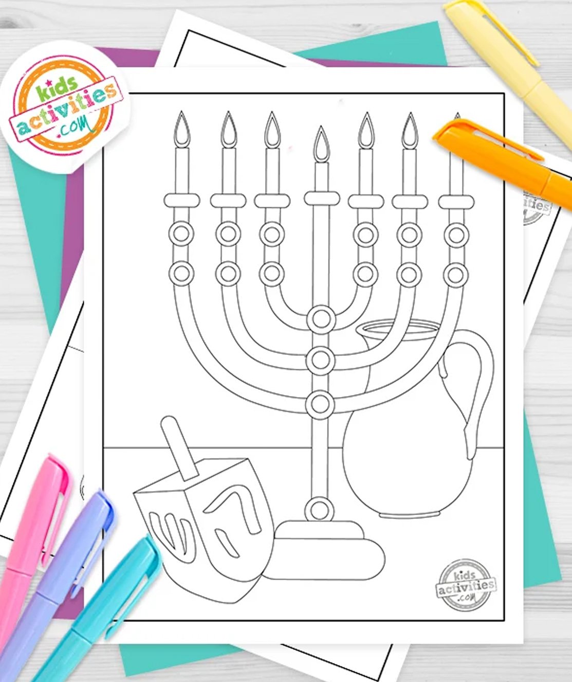 Stack of printed Hanukkah printables on top of green and purple pages, with markers next to them, on top of gray background.