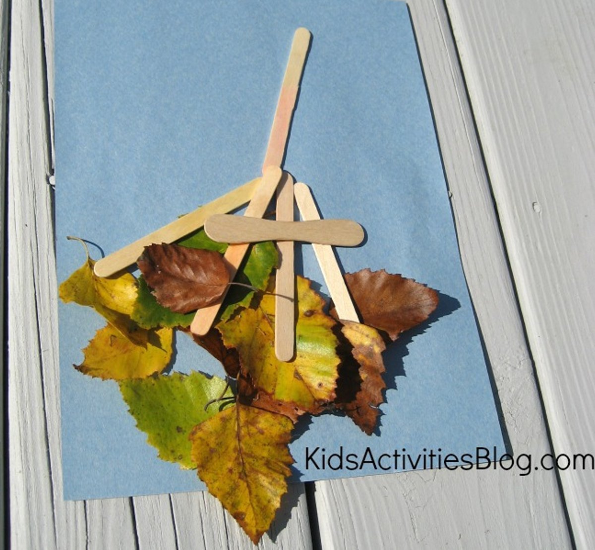 A leaf craft made with leaves and popsicle sticks on top of a blue paper.