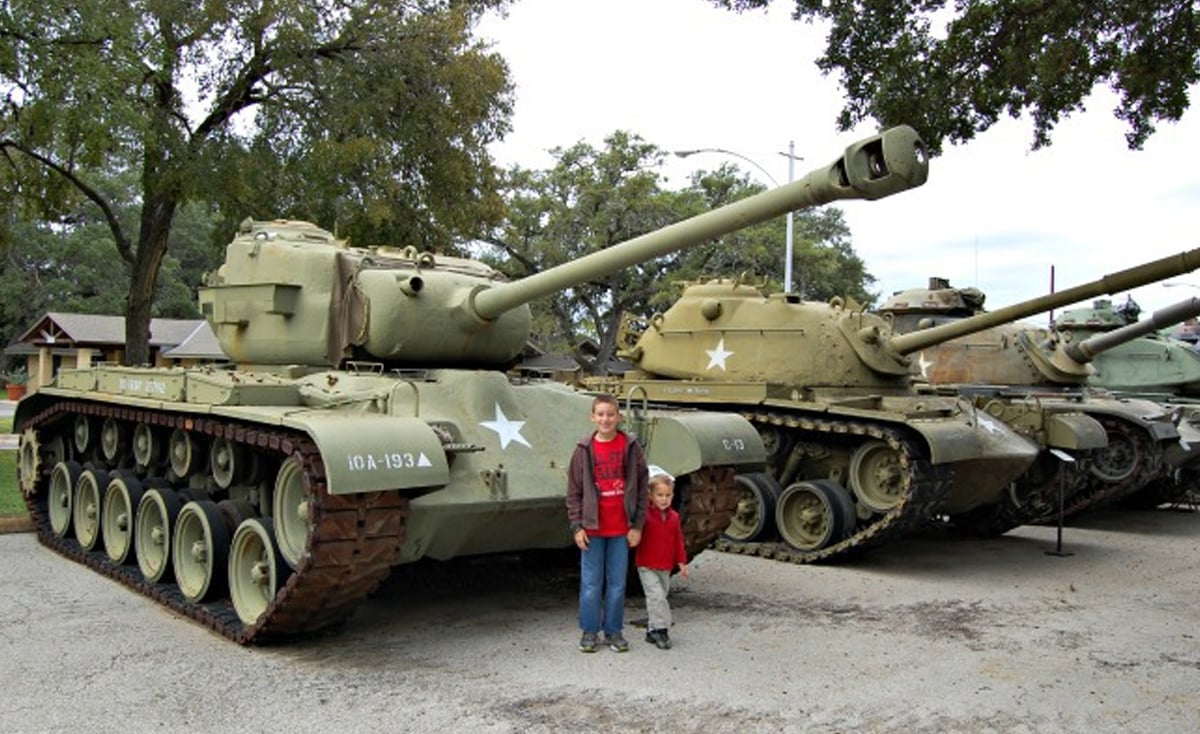 A kid and dad posing in front of two old tanks in a museum.
