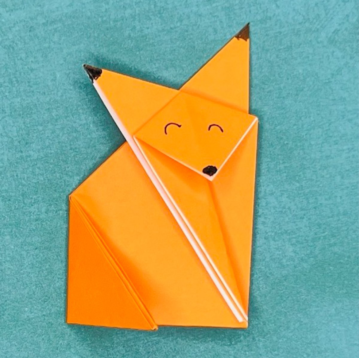 Finished result of a fox origami on top of a green paper.