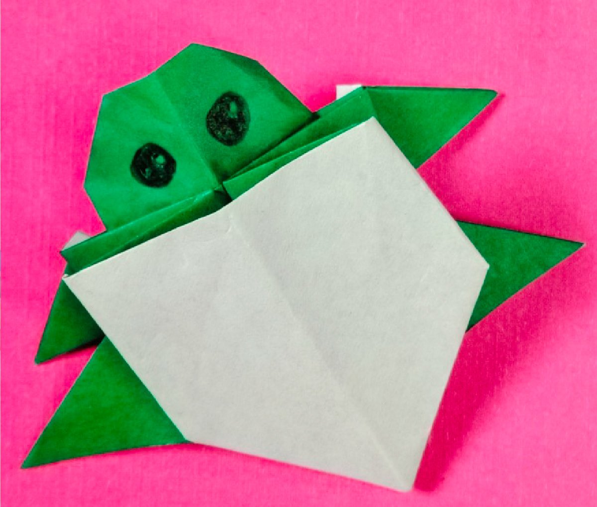 Finished result of a baby turtle origami on top of a pink paper.