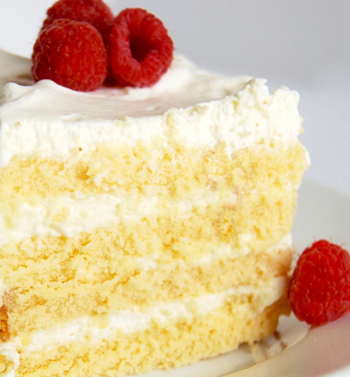 A close-up picture of a vanilla cake with raspberries on top.