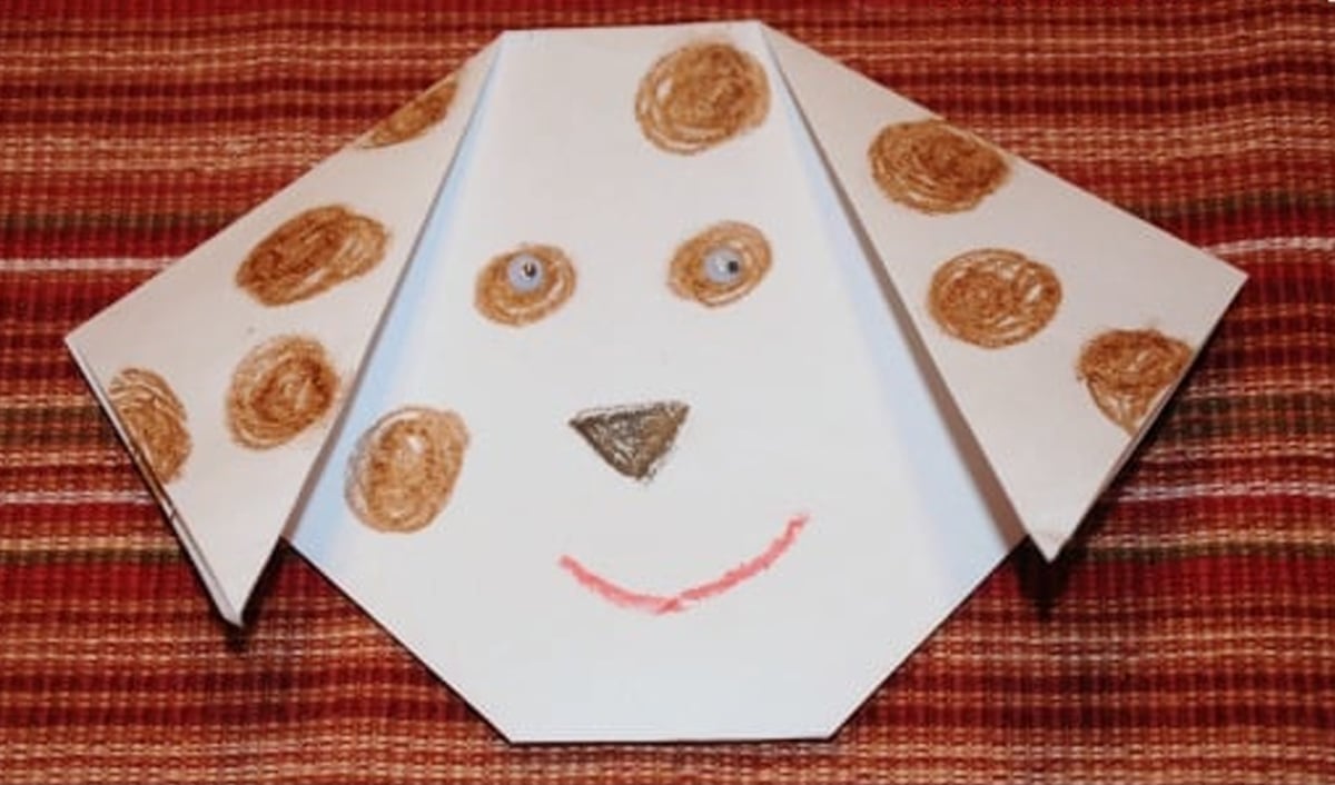 A dog origami craft for kids on top of a wooden table.