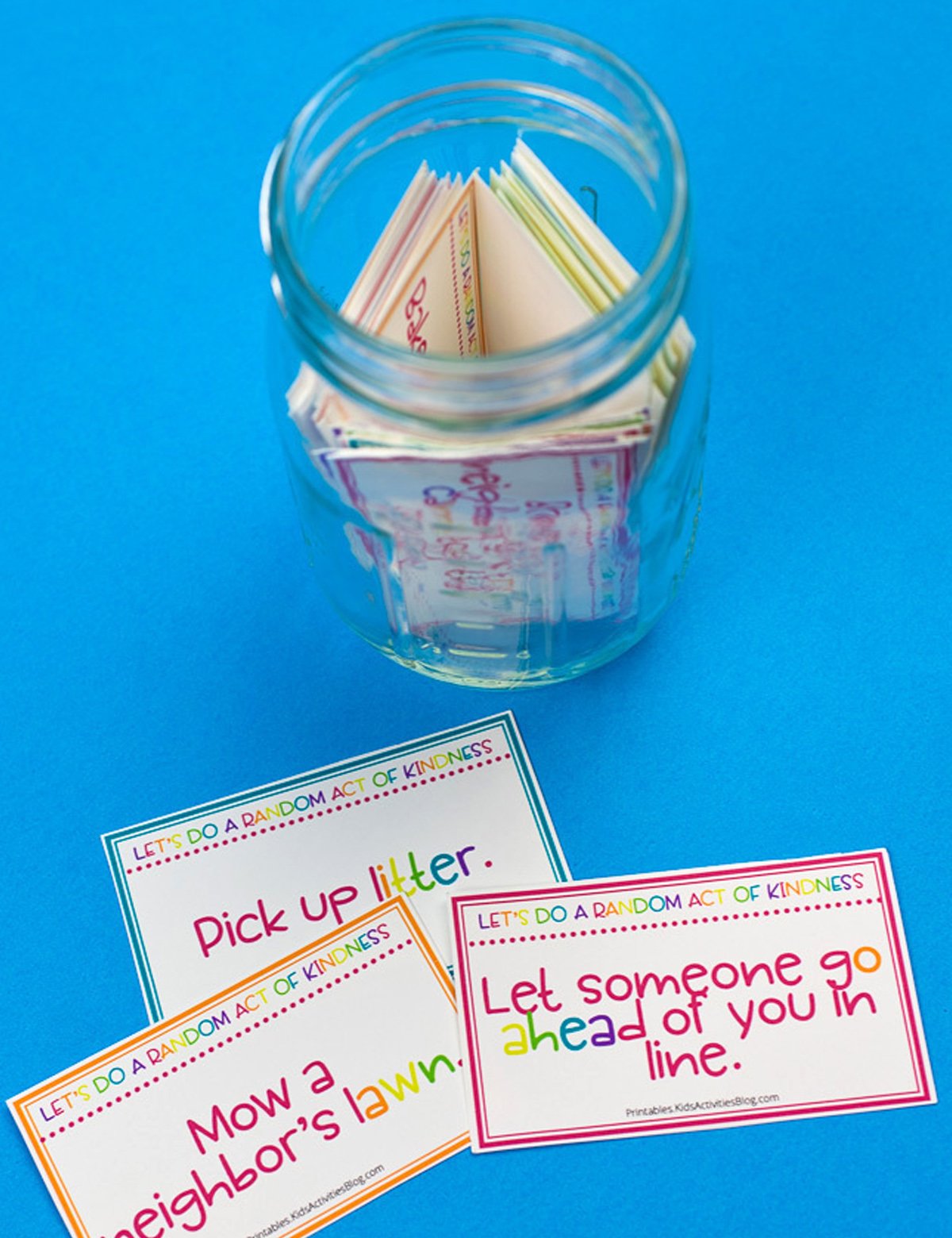 A jar with random acts of kindness cards on top of a blue background.