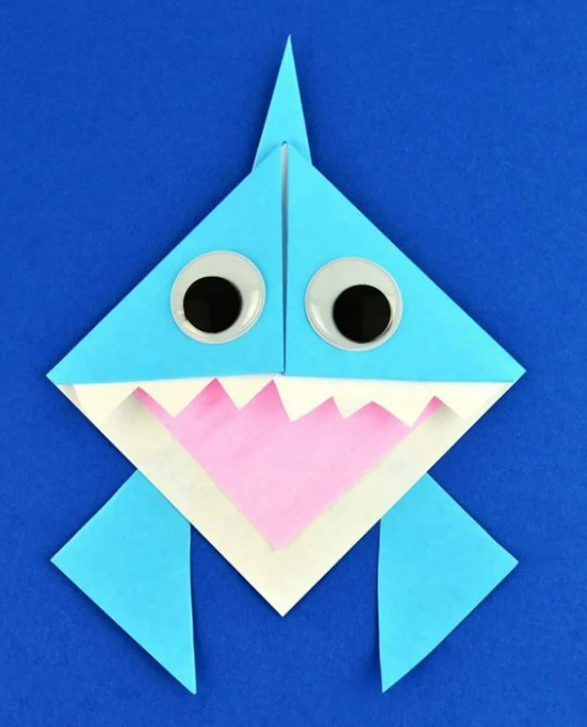 A finished shark origami bookmark on top of a blue background.