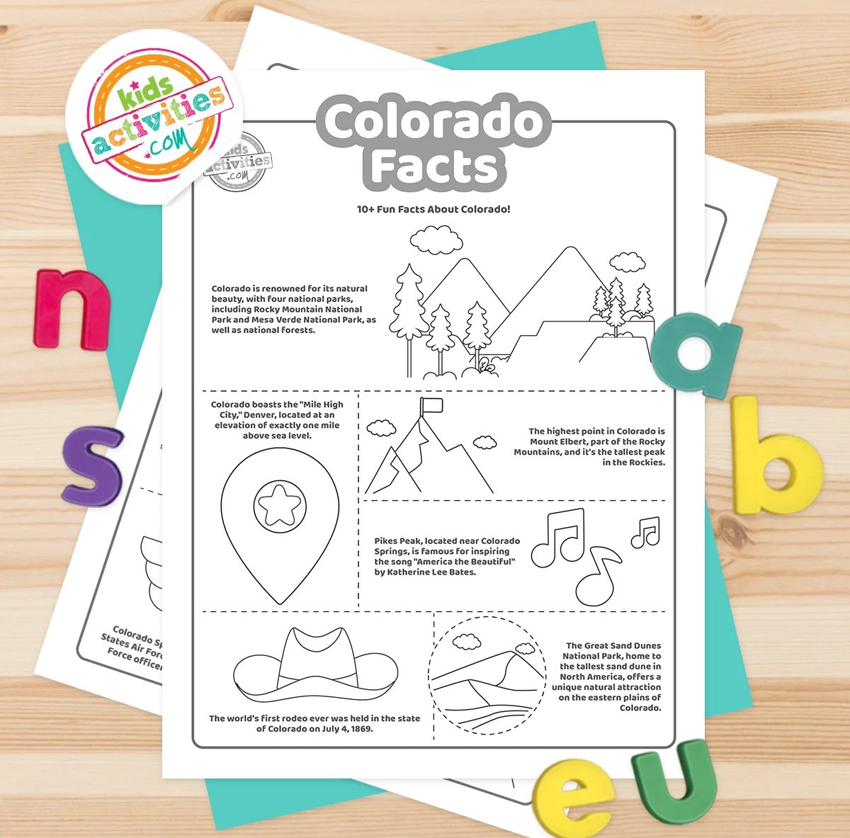 Black and white coloring pages with Colorado facts lying on top of blue-green and purple sheets with assorted crayons on a brown background.