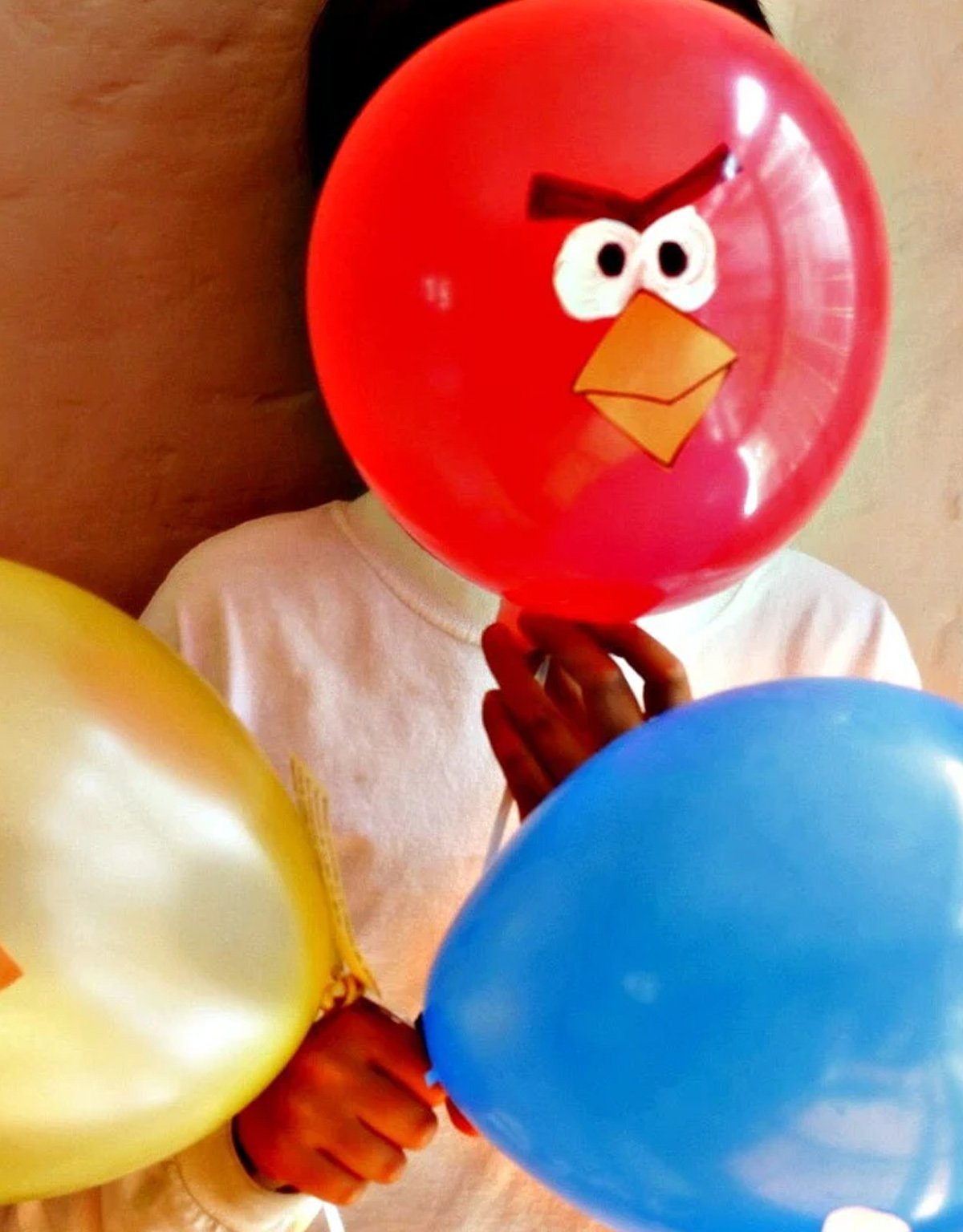 A picture of a kid holding a red balloon painted like a character from angry birds.