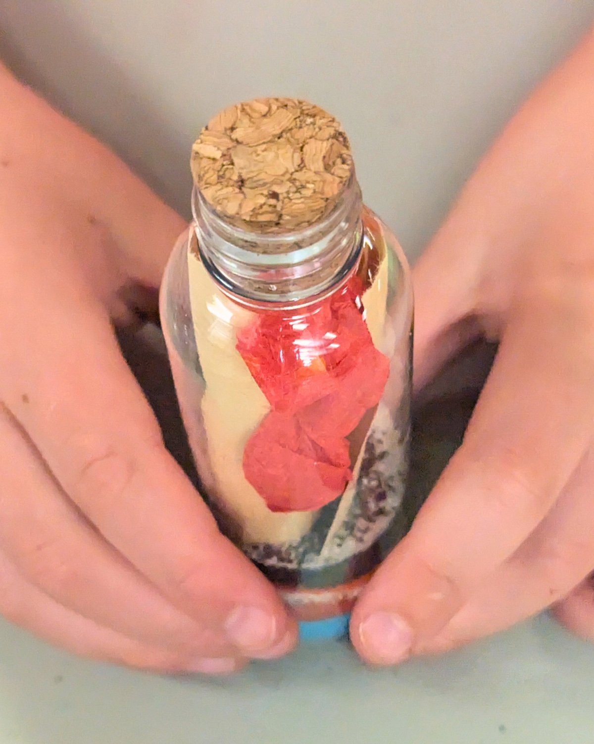Two hands holding a bottle with a message inside, secured with a wine cork.