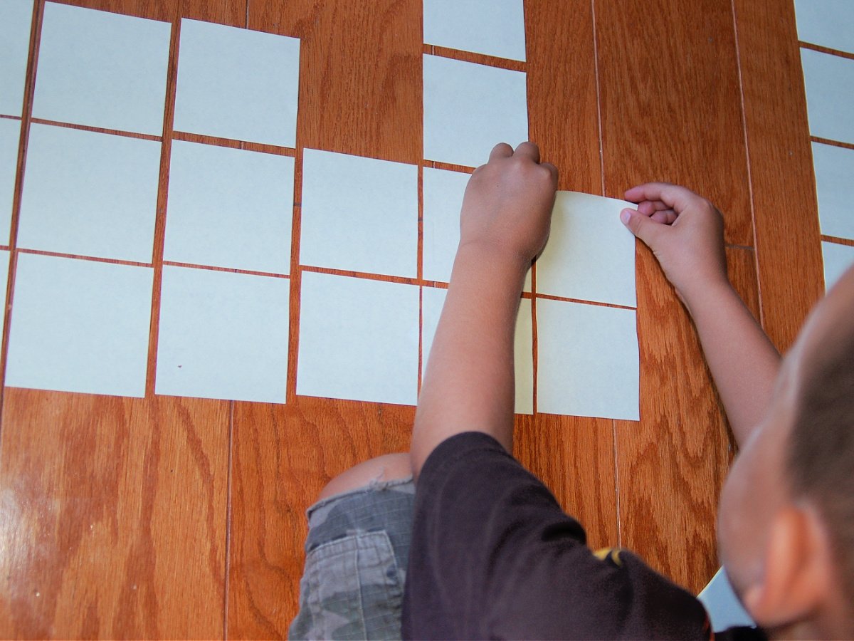DIY Maze- Boy setting up white squares on a wood floor- kids activities blog