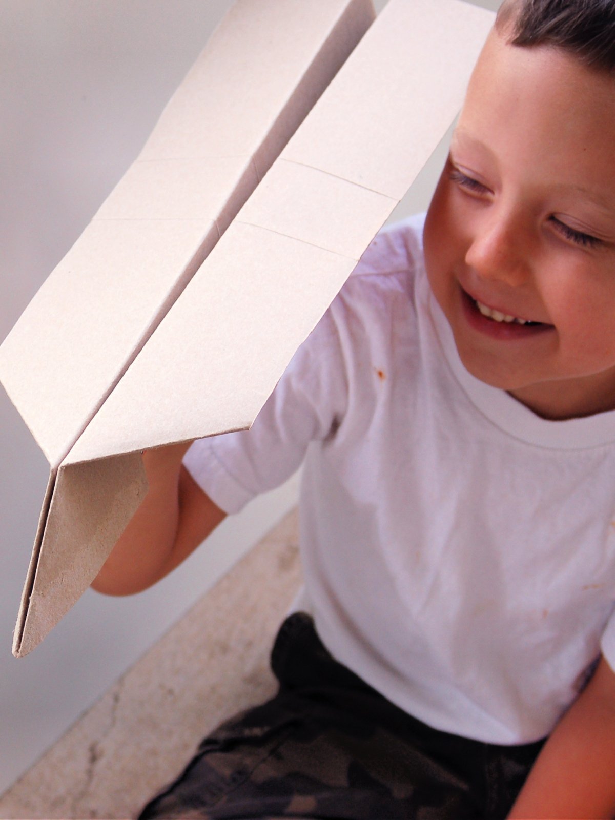 Giant Paper Airplane- Step 5- Boy smiling and holding a white airplane- Kids Activities Blog