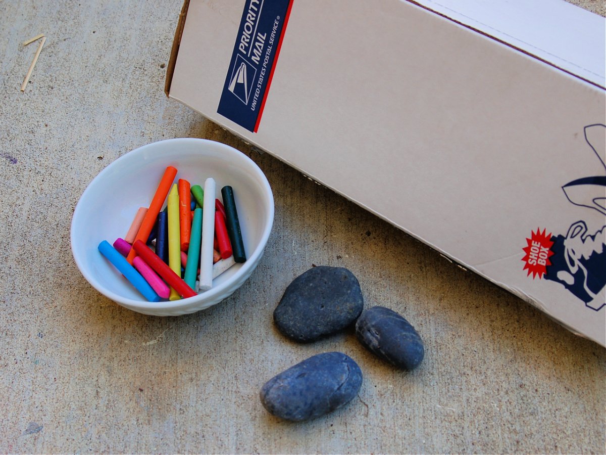 Solar Oven- Supplies- Box with bowl of assortment of crayons, and rocks on pavement- kids activities blog