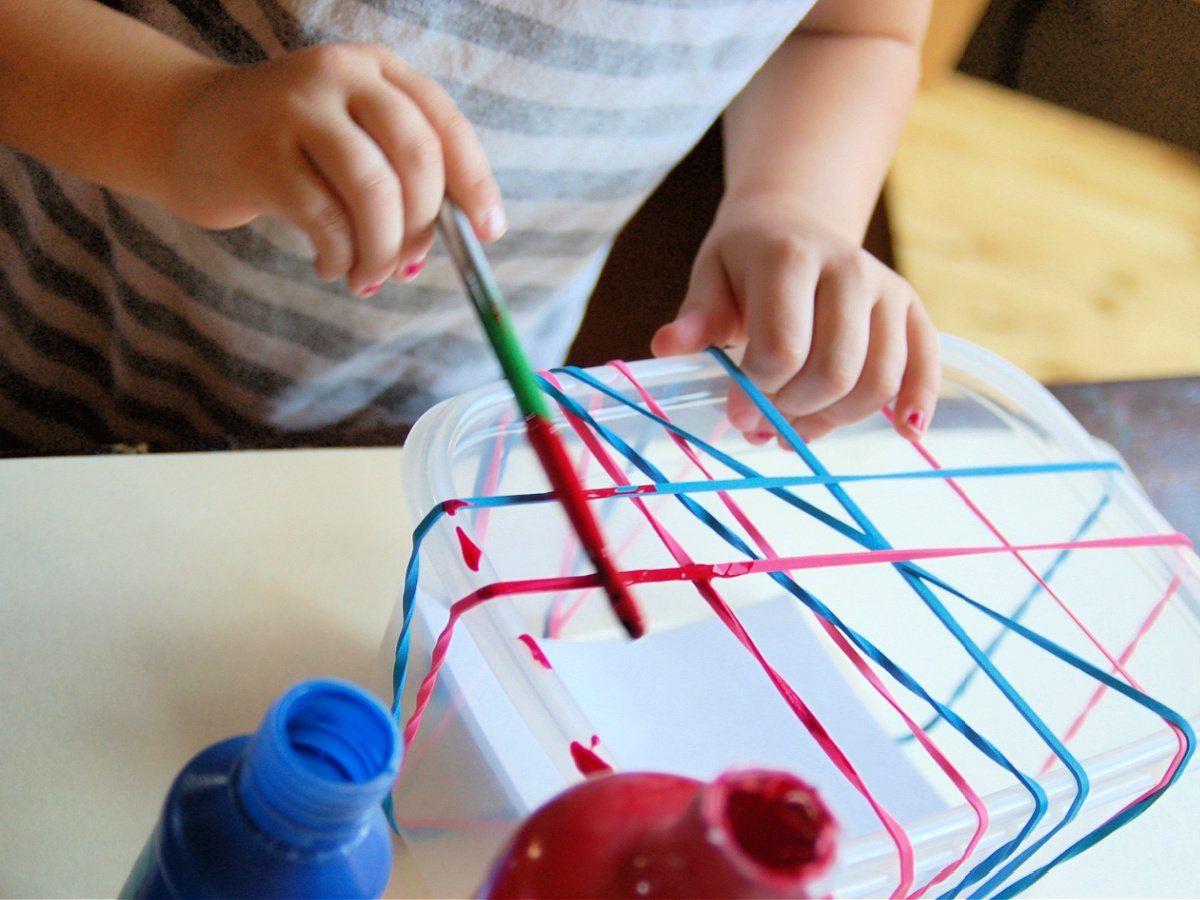 Splatter Paint Art- Step 1- child painting the rubber bands with red paint- kids activities blog