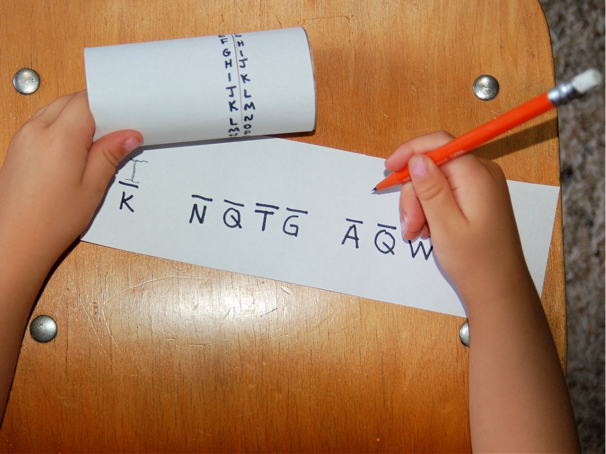 Coded message craft- child with a slip of paper with a coded message, pencil, and decoder- kids activities blog