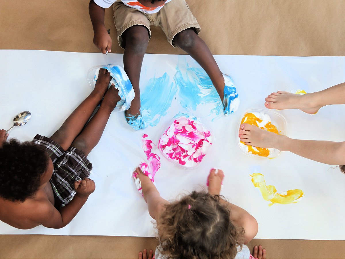 Foot Paint- Step 3- kids dipping feet in shaving cream and paint and painting on the paper- kids activities blog