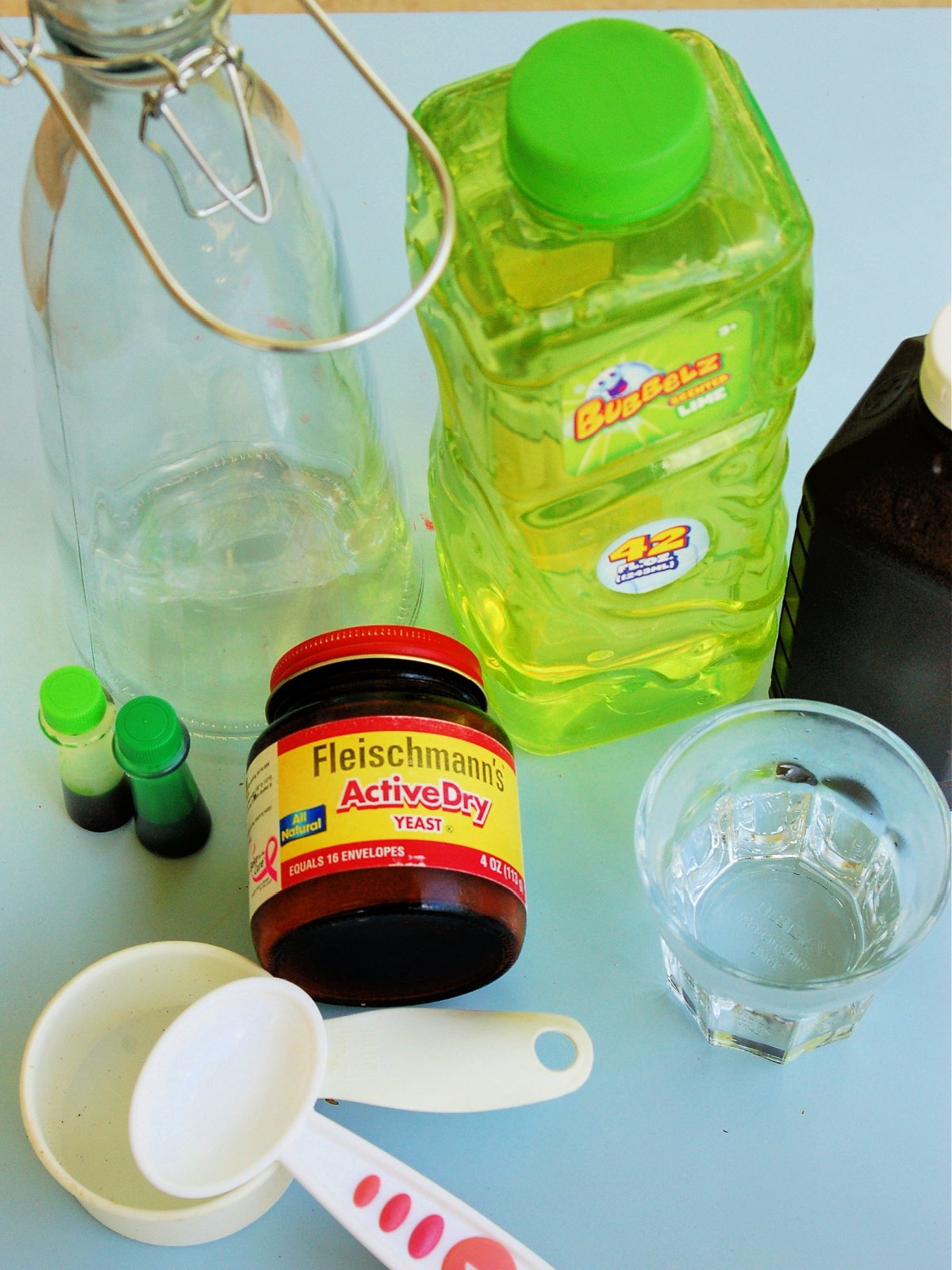 Elephant Toothpaste Supplies- active yeast, bottle, food coloring, measuring cup, spoon, glass, hydrogen peroxide, and bubble solution- kids activities blog