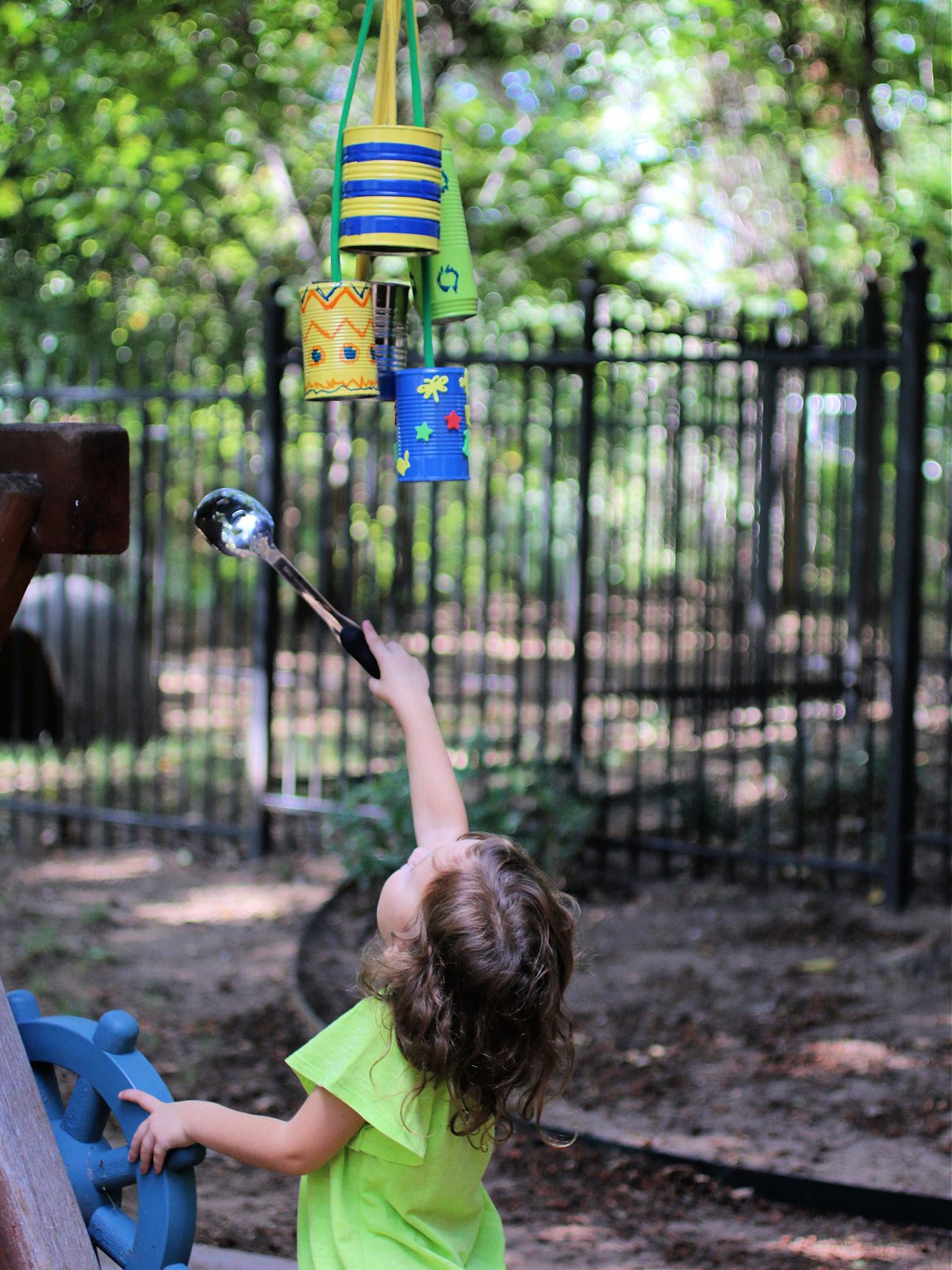 Homemade Wind Chime Craft- child hitting the chimes with a spoon in the park- kids activities blog