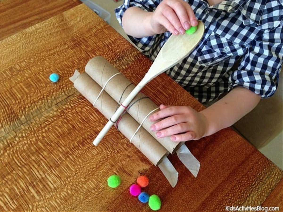 Catapult craft- spoon with paper towel tubes and rubber bands with pom poms- kids activities blog