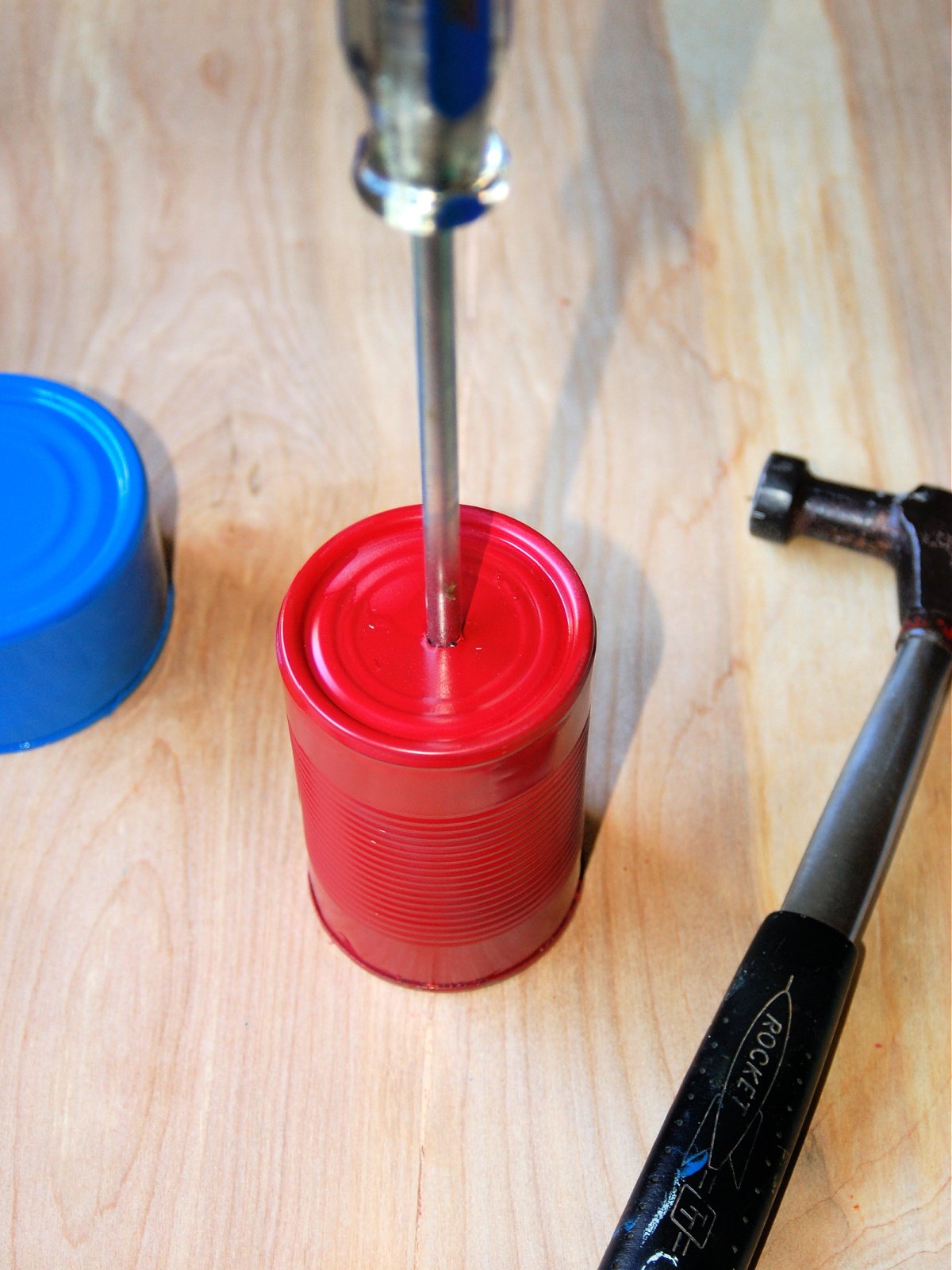 DIY Wind Chime Craft- Step 3- Line up the screw driver and use the hammer to put a hole in the can- Kids Activities Blog
