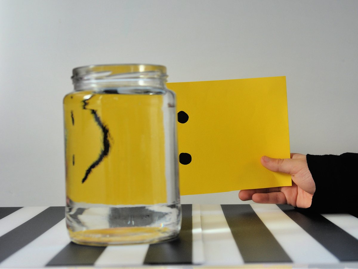 Water illusion- finished- hand holding yellow smiling paper behind water in a jar and looks like a frown- kids activities blog