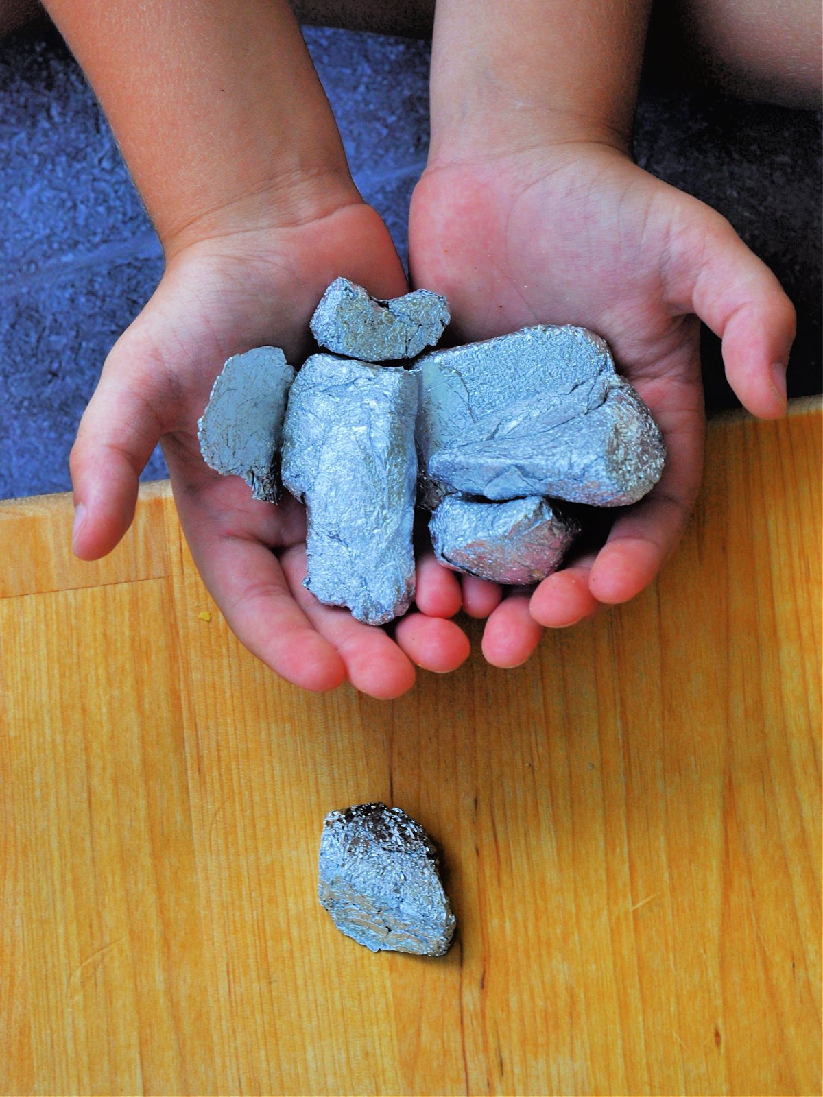 Rock Science Experiment- Step 4- Hands holding lots of aluminum foil rocks- Kids Activities Blog