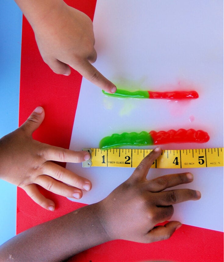 Growing gummies- two kids measuring gummies on a white piece of paper with a tape measure- kids activities blog