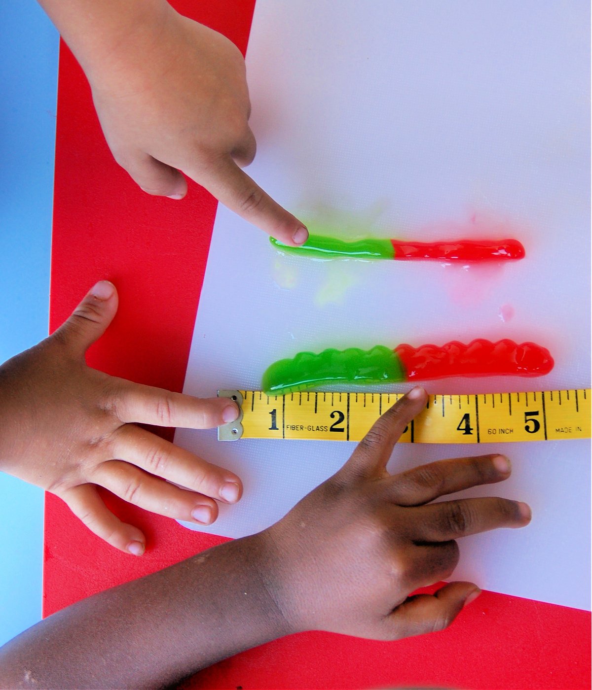 Growing gummies- two kids measuring gummies on a white piece of paper with a tape measure- kids activities blog