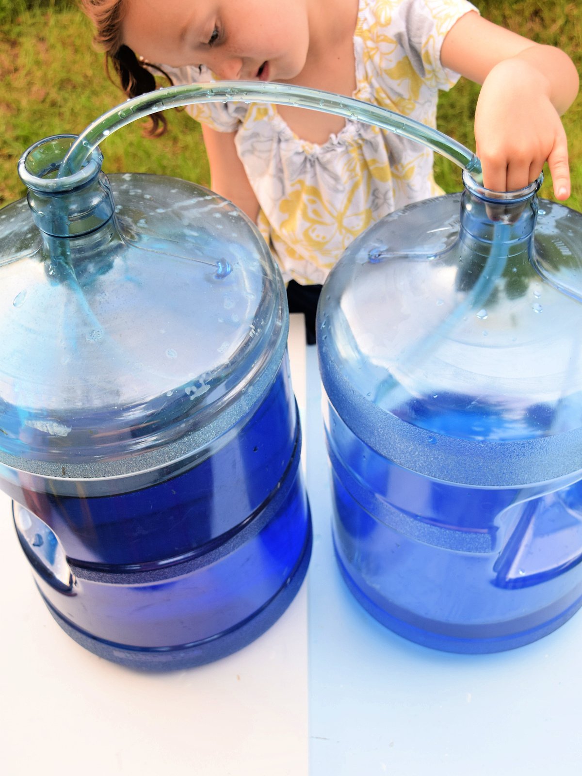 Science Experiment- girl holding clear tubing into the other container outside- kids activities blog