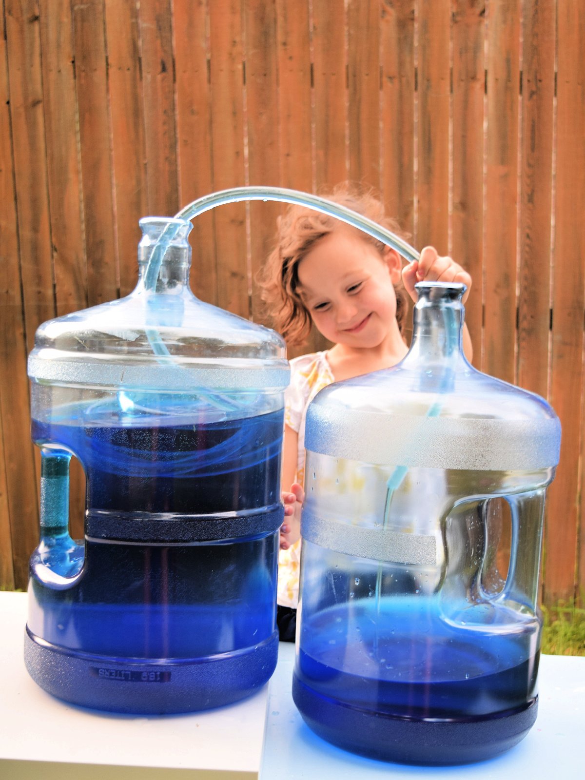 Water Siphon- finished- smiling girl watching water move from one container to the next- kids activities blog