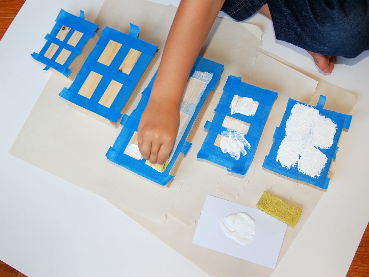 Wooden Town Blocks- Step 3- Child dabbing white paint onto the blocks with a sponge - Kids Activities Blog