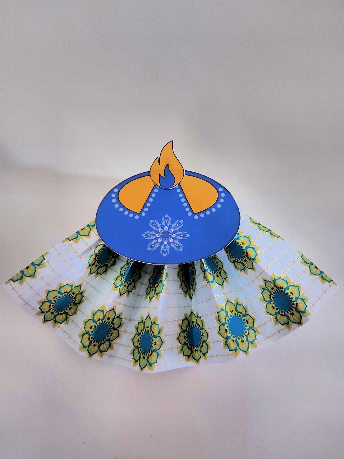 paper diya craft- completed blue diya with green and gold background and blue flame- kids activities blog
