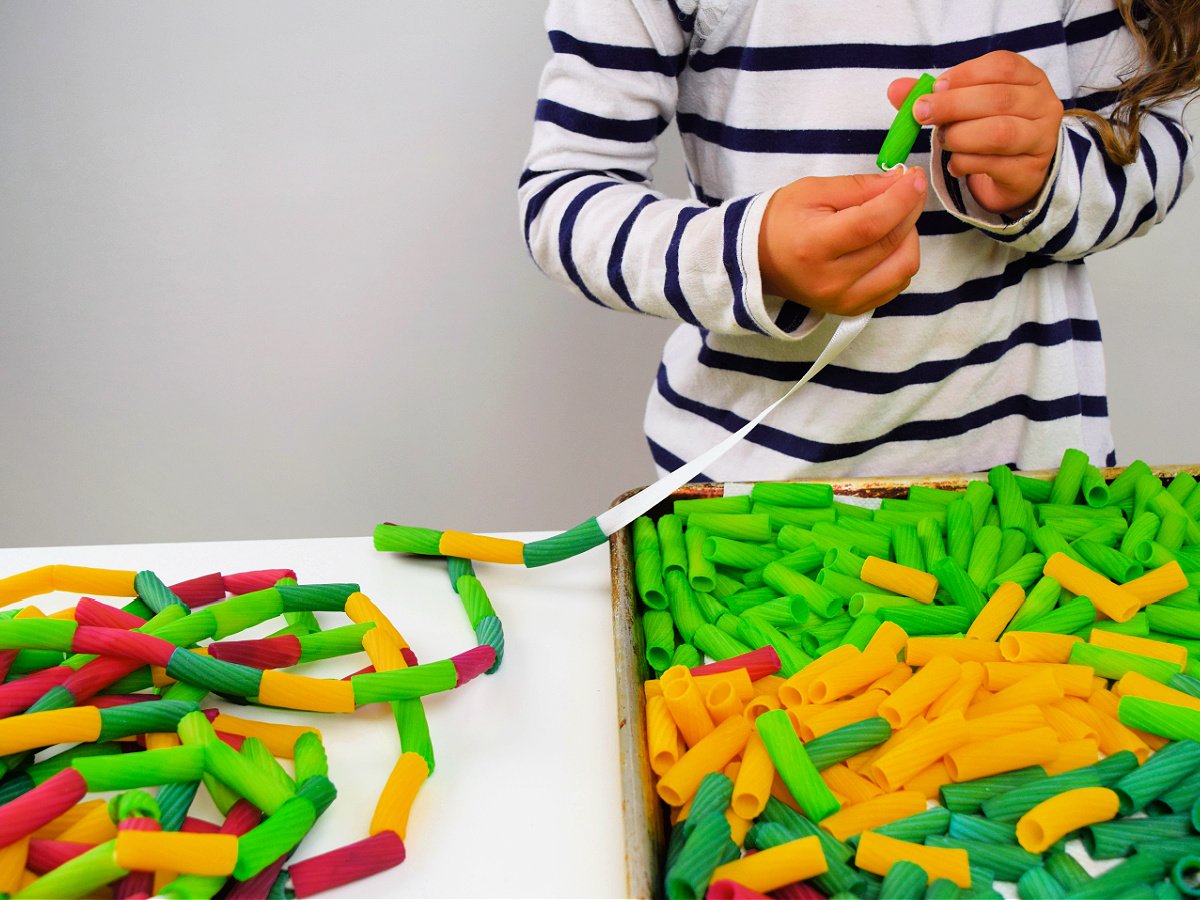 Pasta Fountain Science Experiment- step 1- child threading noodles onto string- Kids Activities Blog