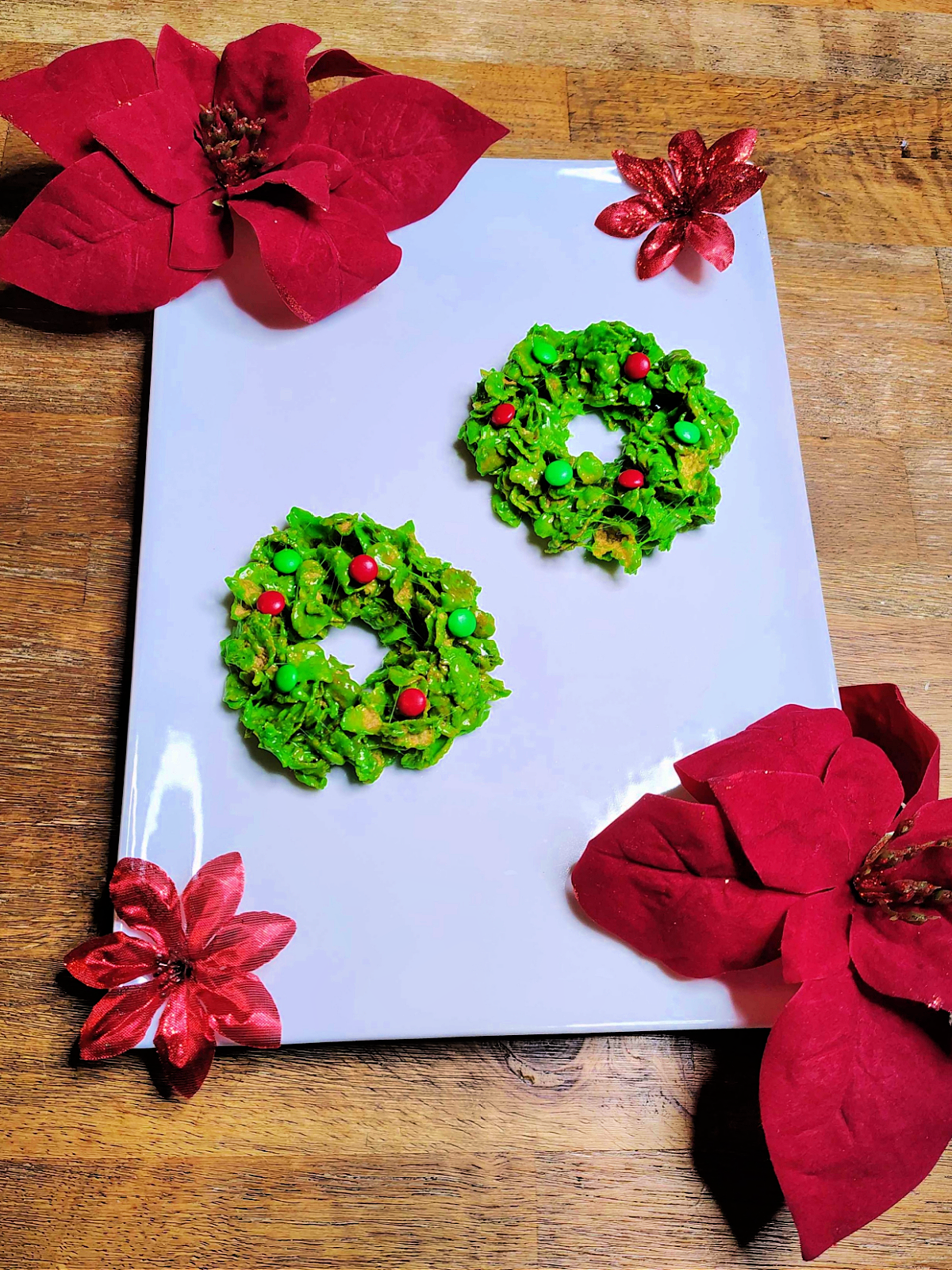 Completed Corn flake Christmas wreathes on a glass plate with red flowers- kids activities blog