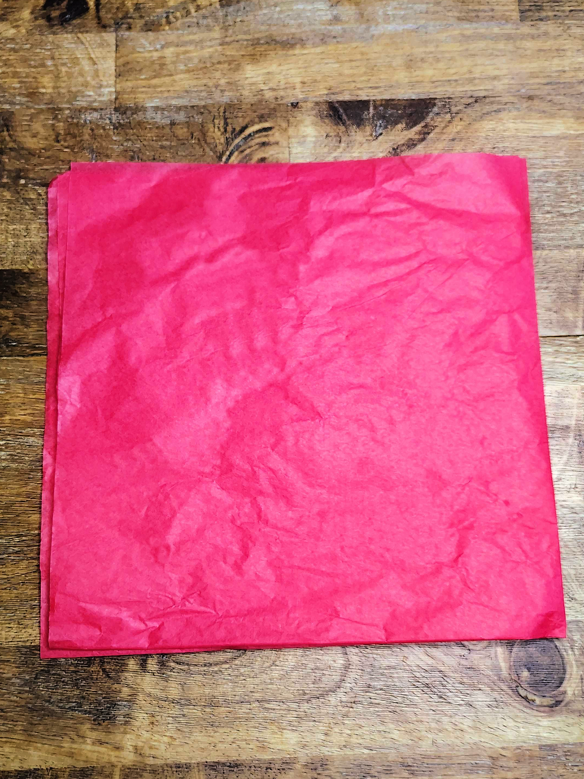 Veterans Day Poppy Craft- Step 1- Fold red tissue paper into a square on wood table - Kids Activities Blog