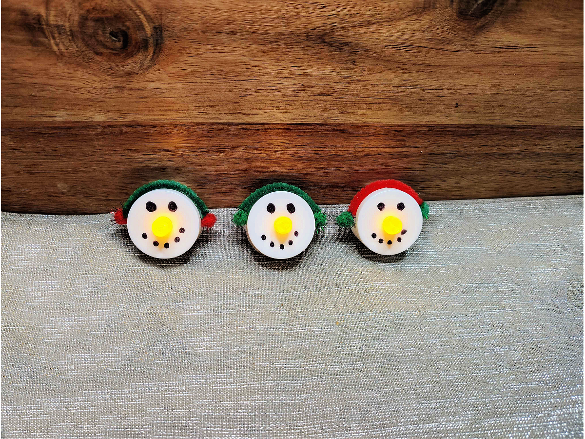 Snowman Craft- Finished - 3 LED candle snowmen with ear muffs and light up noses against a silver and wood background - Kids Activities Blog