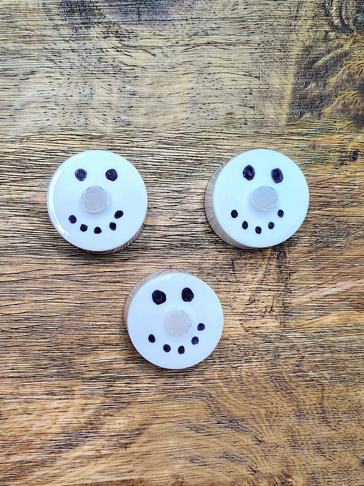 Snowman Craft- Step 1 - eyes and mouths drawn on led candles against wood background - Kids Activities Blog