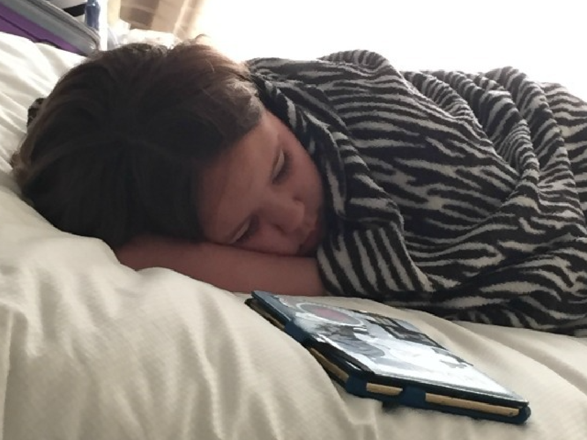 Staycation Ideas- child sleeping on a bed with a tablet- Kids Activities Blog