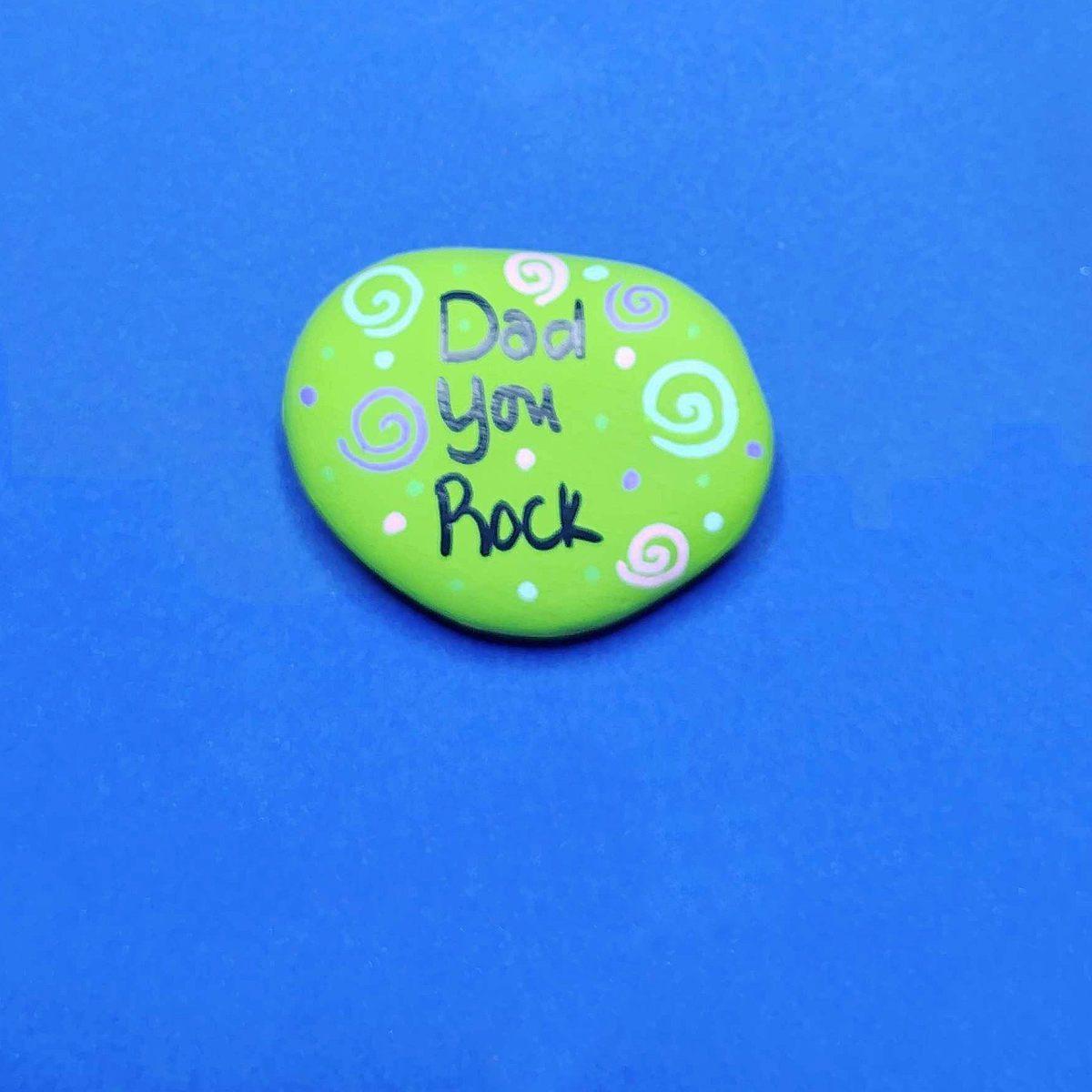 Father's Day Painted Rock Craft- Step 2- Green rock with Dad you rock, blue purple and pink polka dots and swirls-Kids Activities Blog