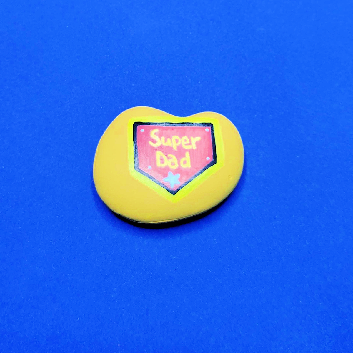 Father's Day Painted Rock Craft- Step 4- Yellow rock with super dad insignia -Kids Activities Blog