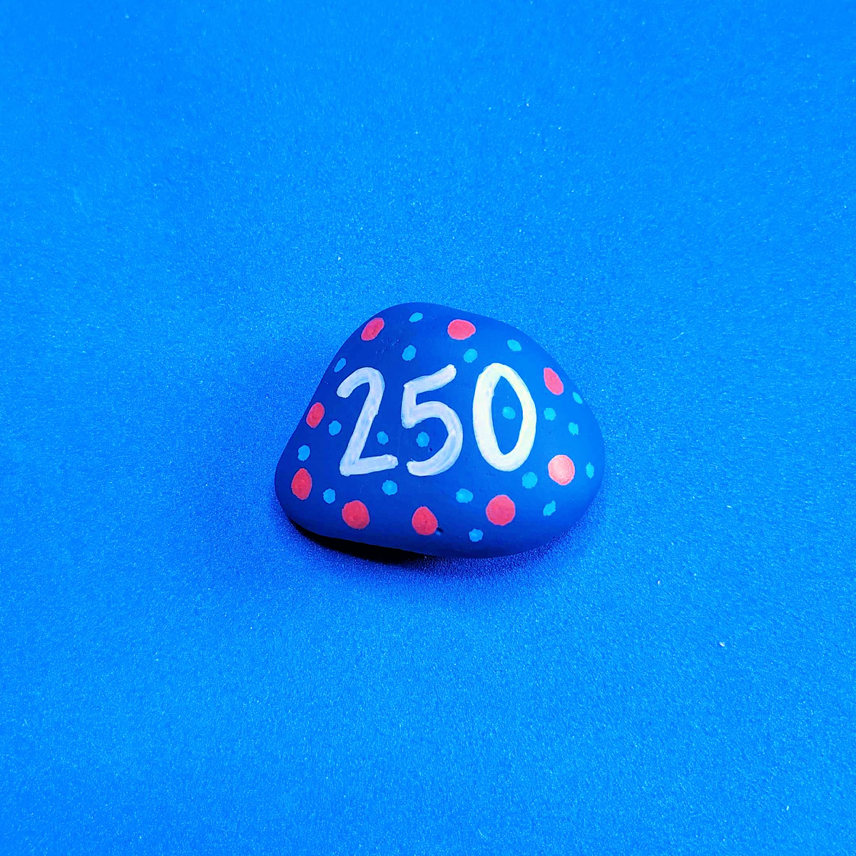 Patriotic Rock Painting Craft- 250 on a blue rock with red and blue dots -Kids Activities Blog