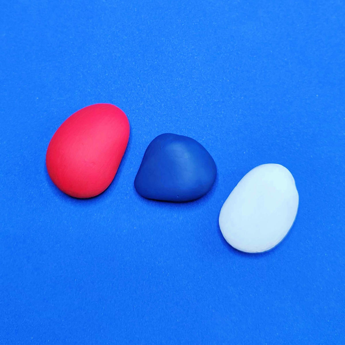 Patriotic Rock Painting Craft- step 1- red white blue rocks on blue background -Kids Activities Blog