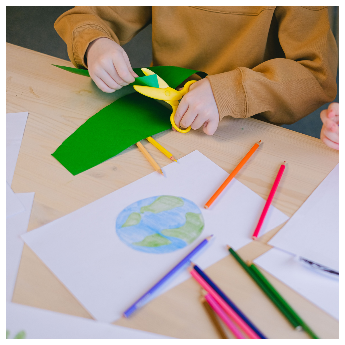 Craft Hacks- child cutting green construction paper with yellow scissors with craft supplies nearby-Kids Activities Blog